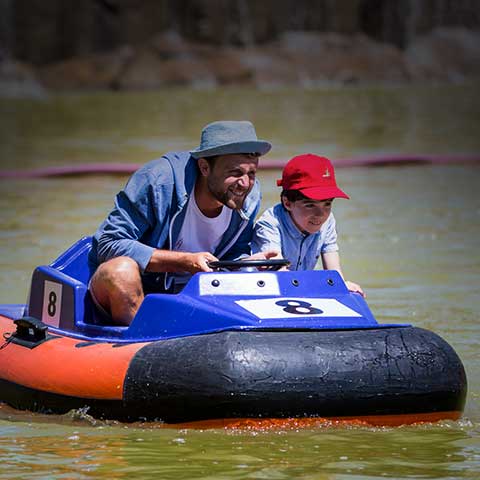 Padre e hijo montados en una de las barcas a motor de la atracción acuática Bumpers, intentando chocar con otra barca.