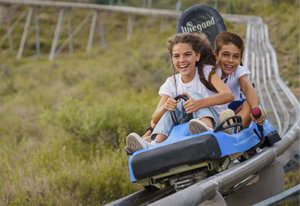Un garçon et une fille descendent les rails du manège de bobsleigh en riant et en s'amusant.